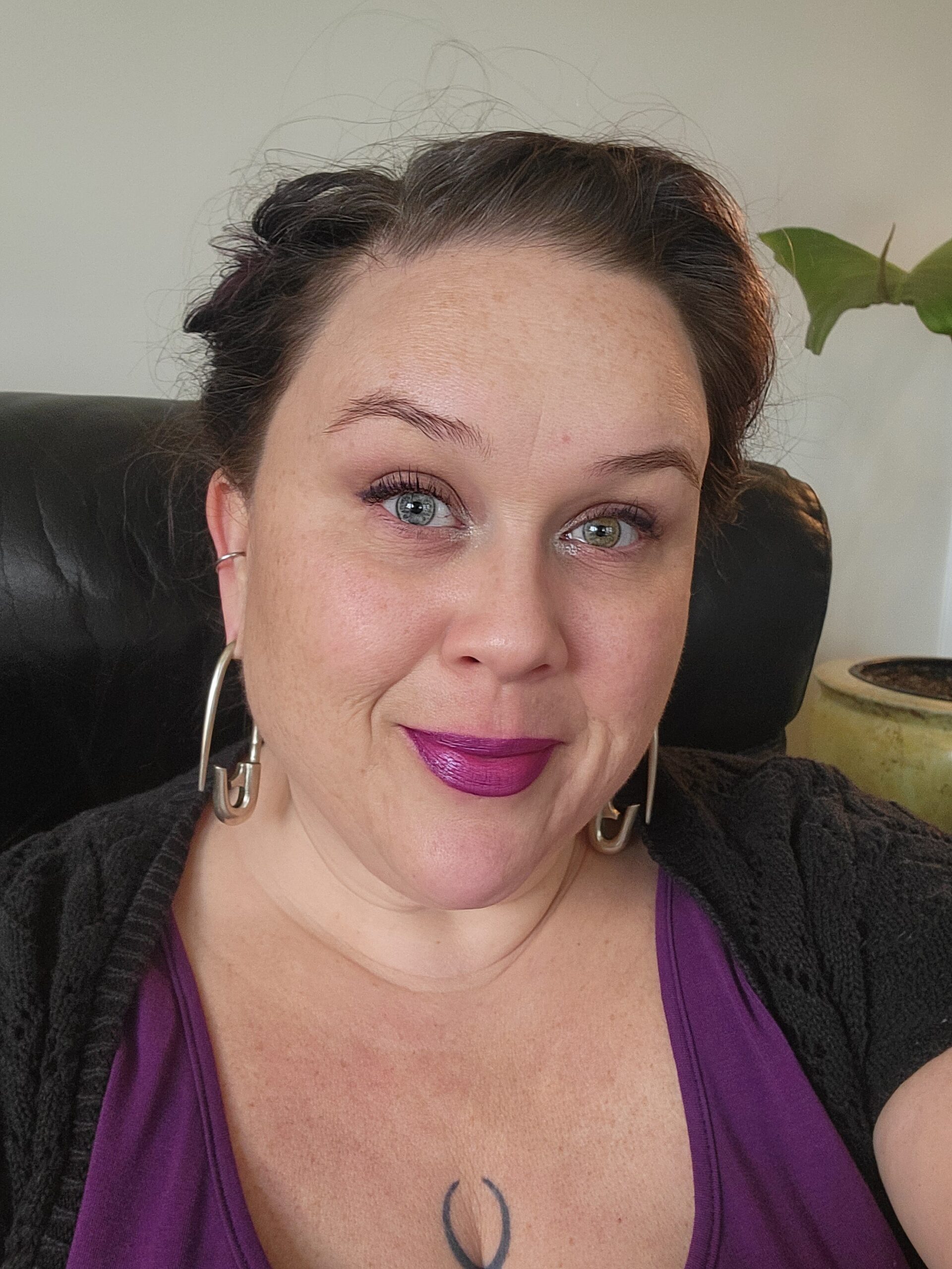 A white-bodied femme-presenting queer therapist wearing a purple top and black cardigan and safety pin earrings A white-bodied femme-presenting queer therapist wearing a purple top and black cardigan and safety pin earrings