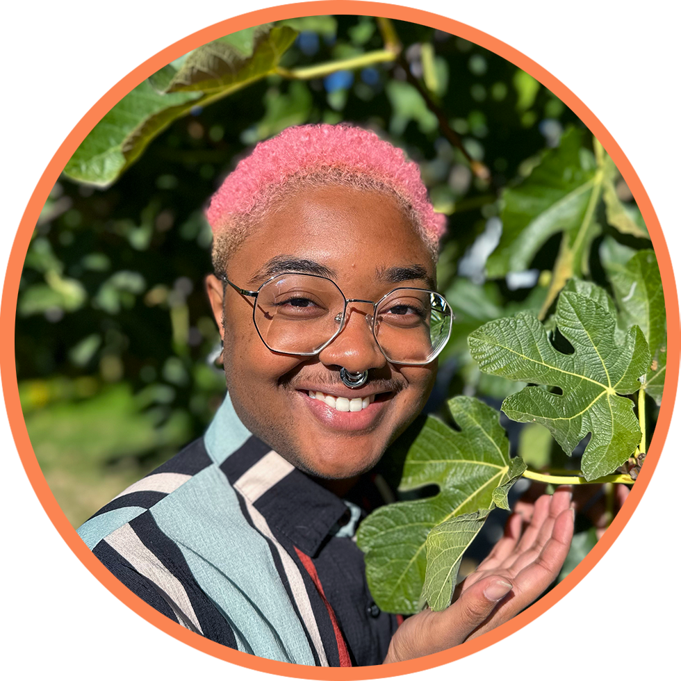 A headshot of Yams with pink hair and glasses in a striped shirt, cupping a large fig leaf in his hand.